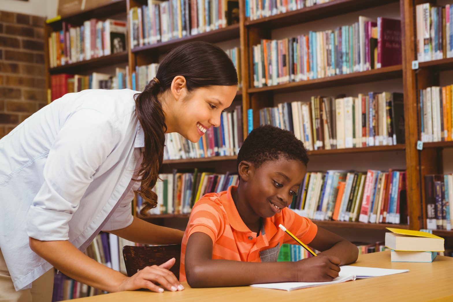 Teacher assisting mixed race boy with homework in library.