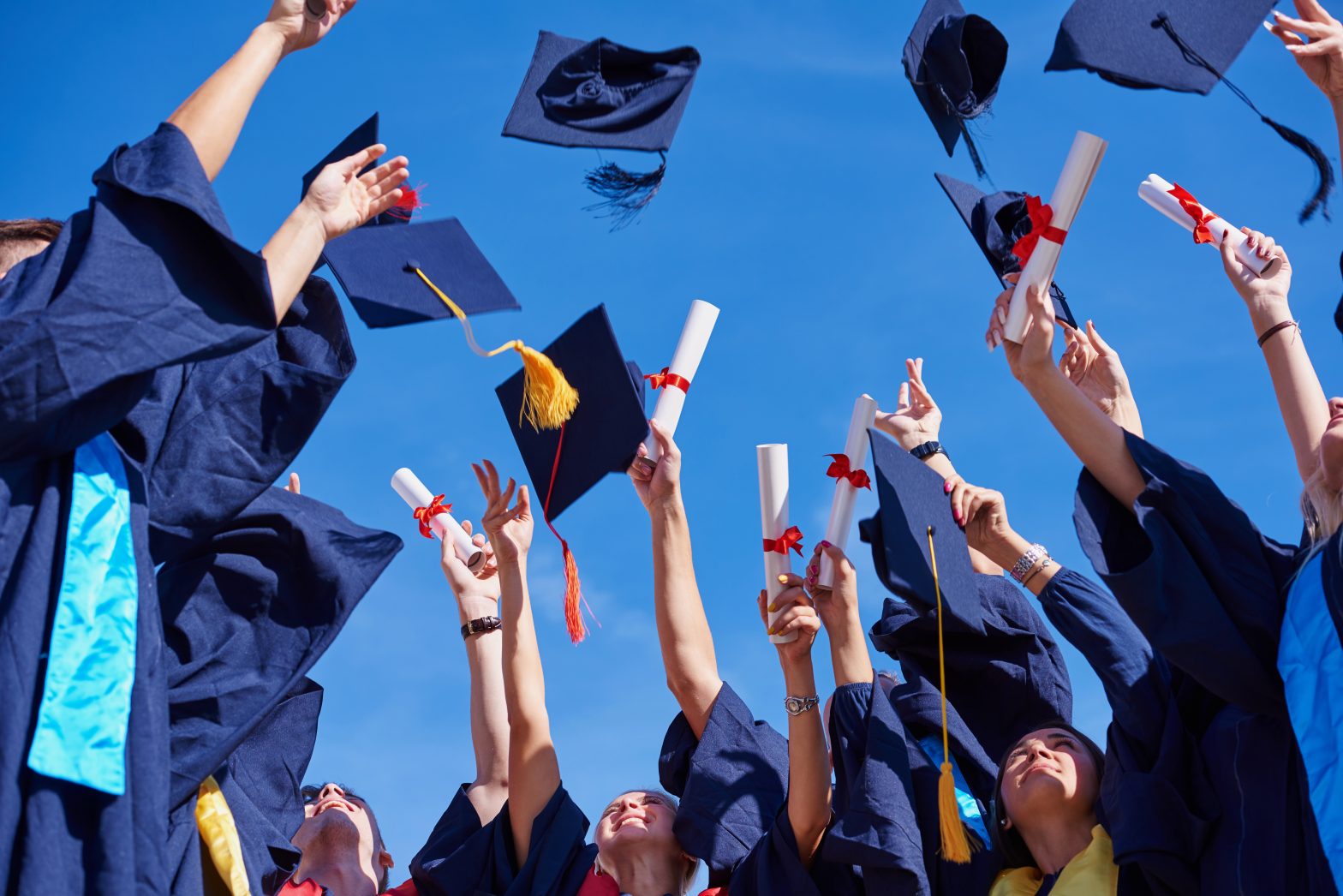 High school student graduates tossing up hats over blue sky.
