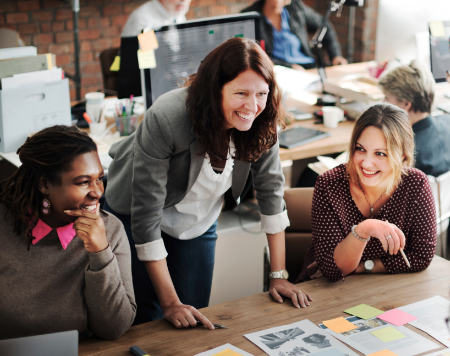 Three individuals engaged in a lively discussion over a laptop, sharing ideas and collaborating in a collaborative work setting.